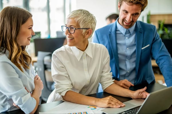 Woman speaks to colleagues while looking at laptop